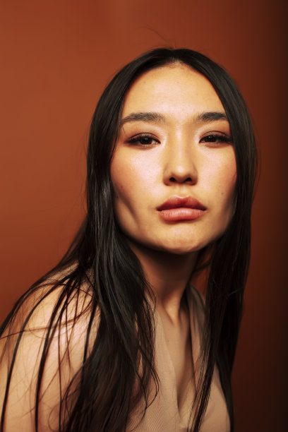 年轻漂亮的亚洲女人开朗的微笑摆姿势在温暖的棕色背景，生活方式的人的概念图片下载