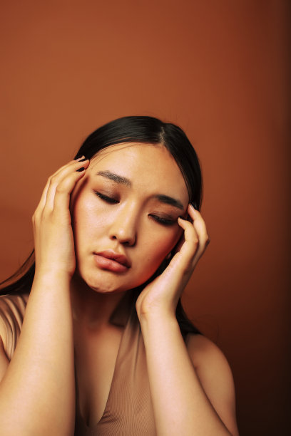 年轻漂亮的亚洲女人开朗的微笑摆姿势在温暖的棕色背景，生活方式的人的概念图片下载