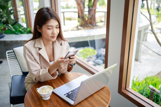 有吸引力的亚洲女商人使用智能手机和笔记本电脑在咖啡店工作。图片下载