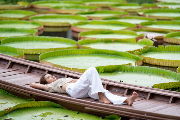 亚洲女孩躺在新的复古木船上的百合荷叶池塘在户外的田野。图片下载