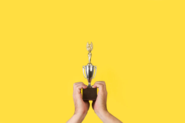 男子手握一个黄色背景的木制底座的金属奖杯图片下载