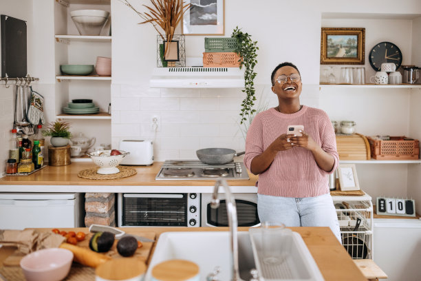 这张照片拍摄的是一名年轻女子在家里的厨房里使用智能手机图片下载