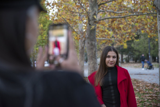 两个女孩用手机在公园里拍照。图片下载