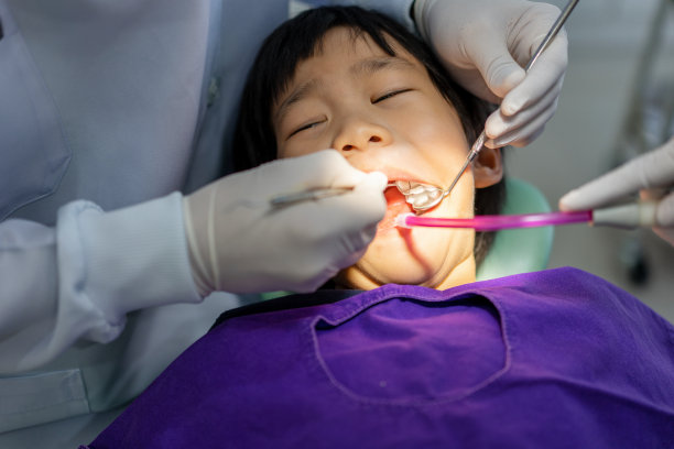 牙科医生的手正在牙科诊所为一名6岁的亚洲小孩治疗牙齿图片下载