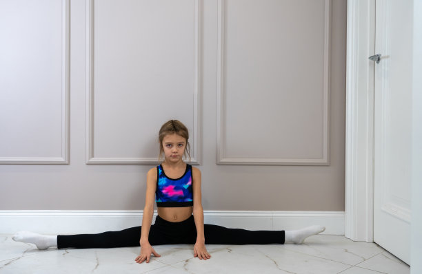 穿着运动服的小女孩在客厅的地板上做劈叉图片下载