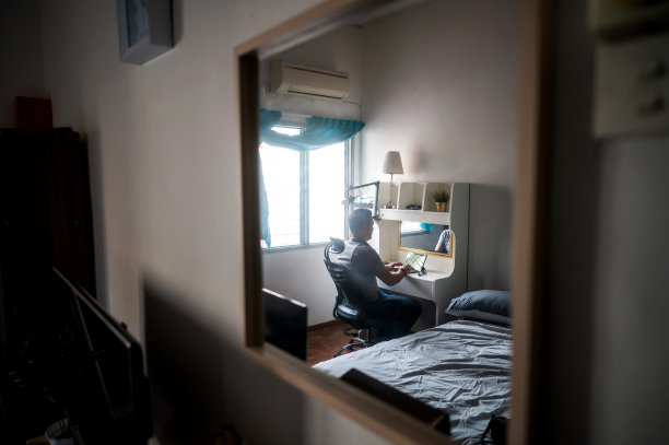 一名亚洲穆斯林中年男子在卧室的办公桌上舒服地用数码平板电脑工作图片下载