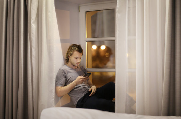 年轻人坐在窗台上玩智能手机图片下载