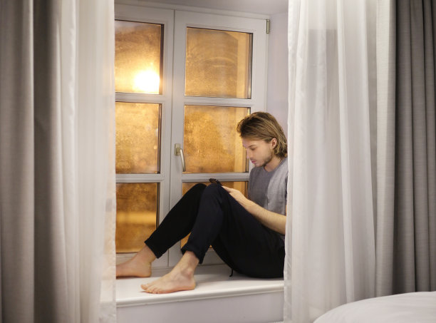 年轻人坐在窗台上玩智能手机图片下载