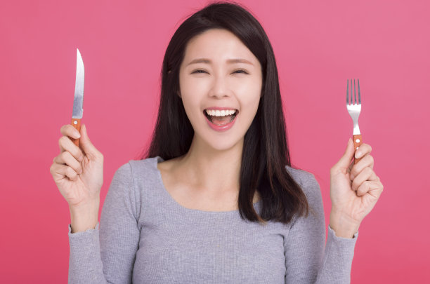 快乐的年轻女子拿着刀叉，等待着美味的饭菜图片下载