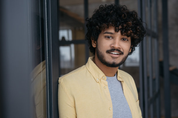 微笑的印度男人站在现代办公室里。英俊成功的亚洲学生看着镜头。教育的概念图片下载