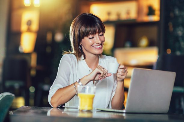 一个漂亮迷人的女人在咖啡厅拿着笔记本电脑喝咖啡图片下载