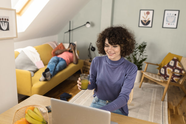 快乐的年轻女人在网上工作她的男朋友在沙发上休息图片下载