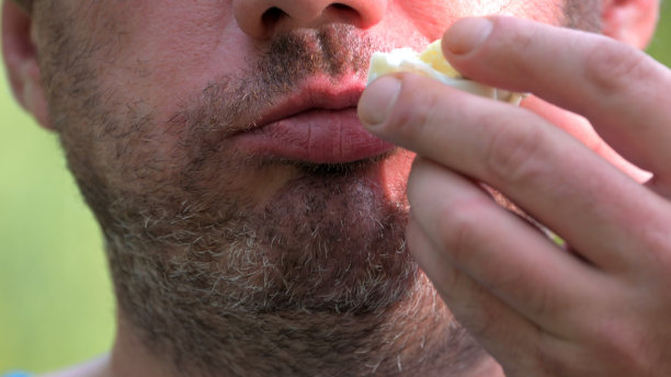 一个没刮胡子的男人在绿色的自然背景下吃煮鸡蛋。有选择性的重点图片下载