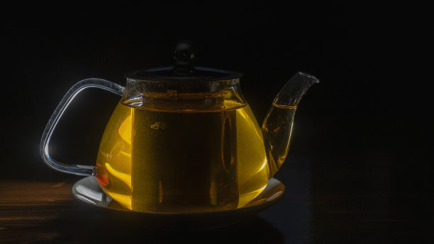 黑色背景的茶玻璃茶壶。木桌上有绿茶和茶壶。广告构成。图片下载