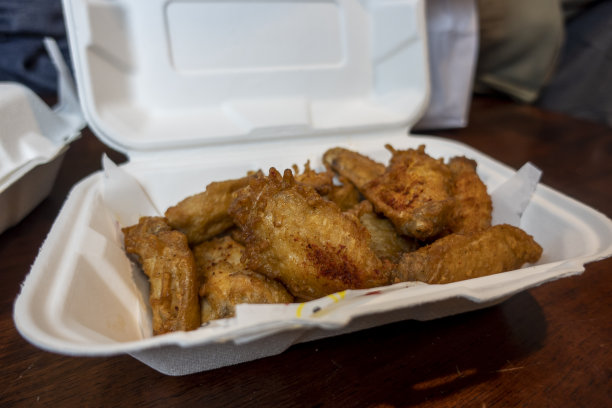 近距离观察，选择性地关注厨房桌子上一份装在白色泡沫保鲜盒里的酥脆鸡翅图片下载
