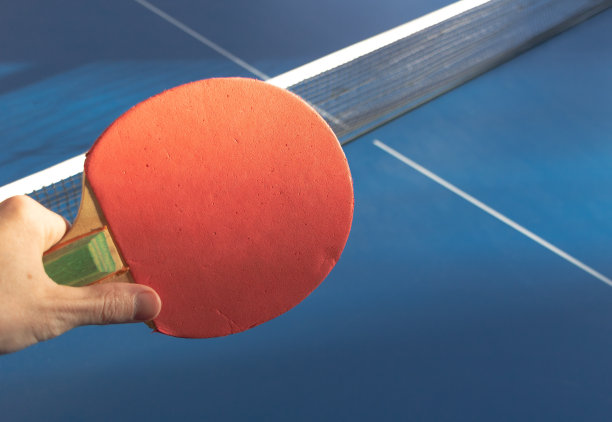 蓝色网球桌上手中红色乒乓球拍的特写图片下载