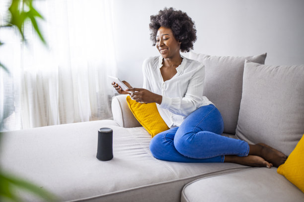 黑人妇女正在把手机连接到她的虚拟助手智能音箱上。图片下载