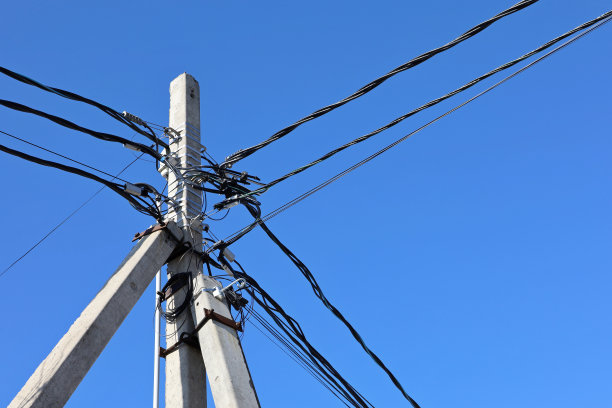 在蓝色的天空背景下，电线和电容器纠缠在一起的电力线柱图片下载