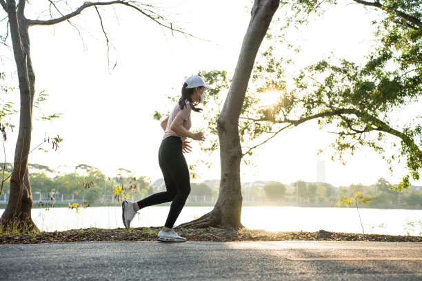 亚洲年轻运动女性戴着面具在大街上公园跑步。美丽的运动员女孩在运动服装锻炼慢跑锻炼户外健康在流行病期间傍晚日落在花园。图片下载