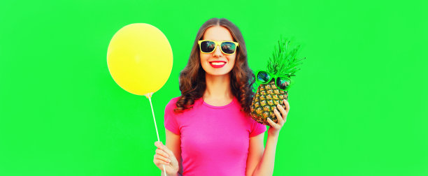 快乐微笑的年轻女子的夏天肖像与菠萝和黄色的气球在绿色的背景图片下载