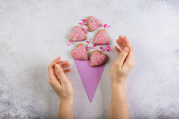 粉红色的心形纸制玉米饼干，就像情人节或母亲节自制的花束。女人的手图片下载