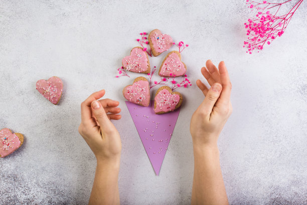 粉红色的心形纸制玉米饼干，就像情人节或母亲节自制的花束。女人的手图片下载