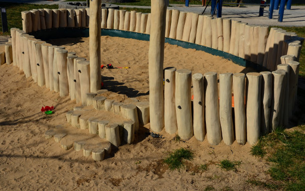 沙箱里的原木低栅栏将球场上的游戏区域与沙地上的路径分隔开来。一排圆形的柱子，沙子覆盖的楼梯，草坪，儿童玩具图片下载