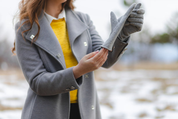 一个年轻漂亮的女孩穿着灰色的外套，在森林外面戴上手套的特写镜头图片下载