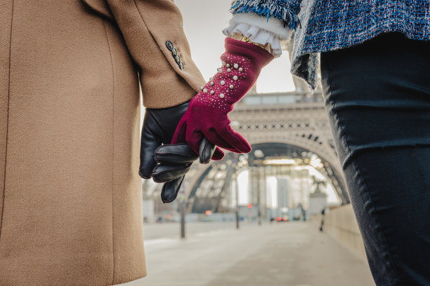在巴黎埃菲尔铁塔前，一对情侣手牵着手，戴着手套图片下载