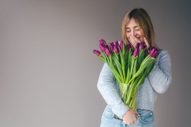 一个年轻女子的肖像与一束郁金香在灰色的背景。图片下载