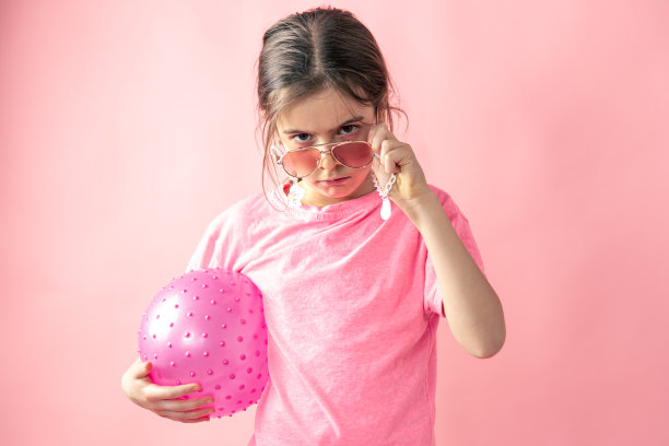 时尚的小女孩，戴着太阳镜，粉色背景上有一个球。图片下载