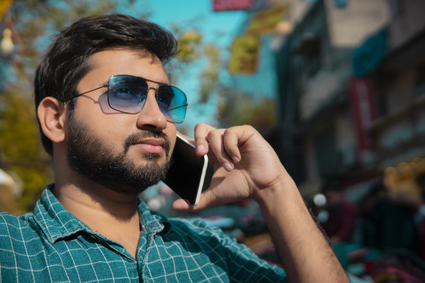 一个戴着墨镜的帅哥在市场上用智能手机聊天。图片下载