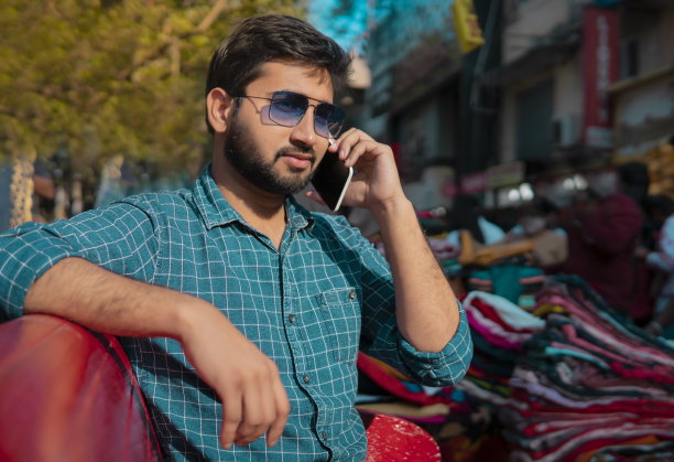 一个戴着墨镜的帅哥在市场上用智能手机聊天。图片下载