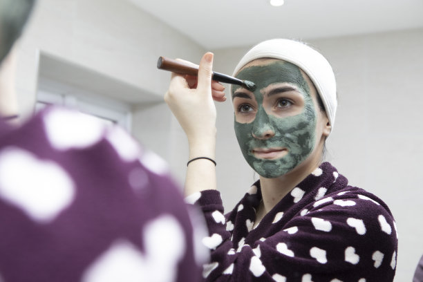 一名年轻女子在家用浴室的镜子前用刷子刷绿色面膜图片下载