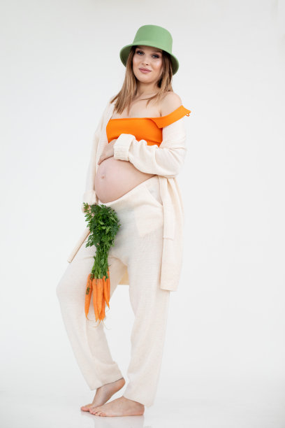 垂直照片明亮的光脚微笑迷人的女人在绿色的帽子停留，一束胡萝卜。怀孕拔毛图片下载