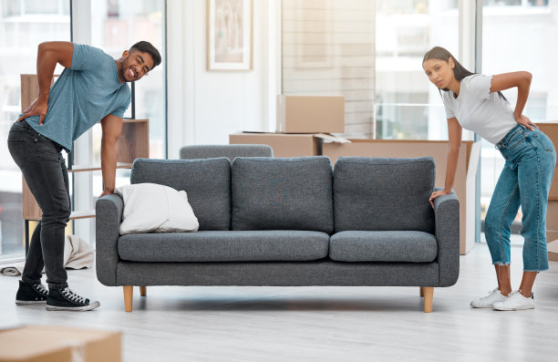 这是一对年轻夫妇在搬动家里的沙发后背部疼痛的全景式照片图片下载