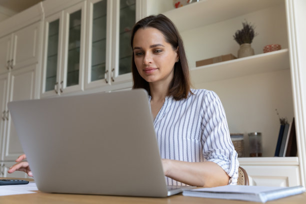 女人坐在桌子旁看着笔记本电脑，在计算器上计算图片下载