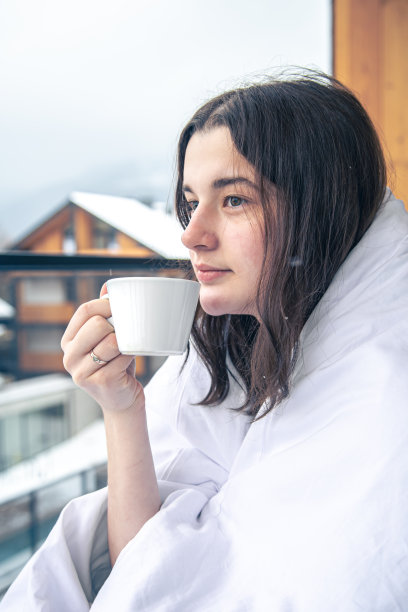 冬天的山里，一个年轻的女人在阳台上喝着咖啡。图片下载