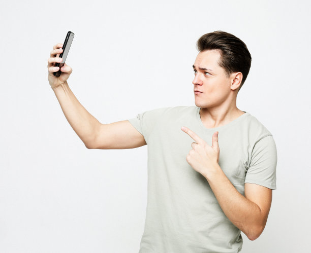 一名年轻英俊的男子穿着t恤，拿着手机自拍图片下载