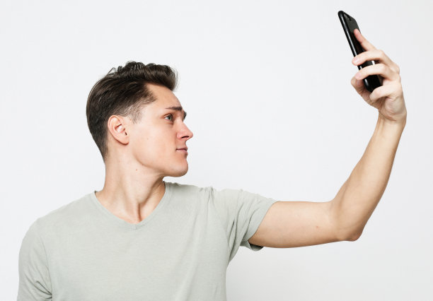 一名年轻英俊的男子穿着t恤，拿着手机自拍图片下载