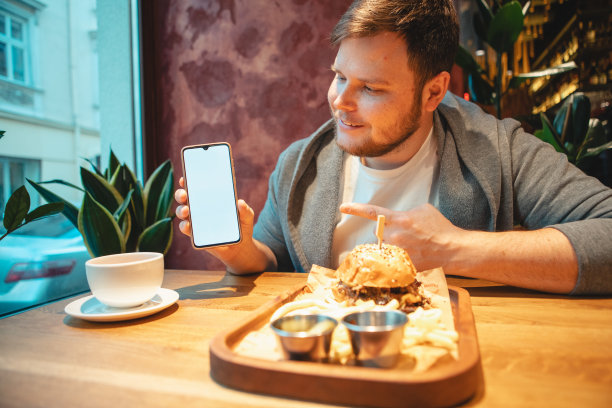 一个男人在咖啡馆拿着手机吃汉堡图片下载