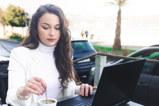 年轻的白人女性一边在海边的露台上喝咖啡，一边用笔记本电脑工作。图片下载