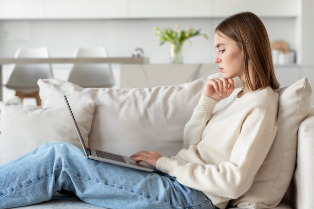 一个年轻漂亮的女人，穿着休闲的衣服，拿着笔记本电脑，坐在一个现代室内的沙发上。图片下载