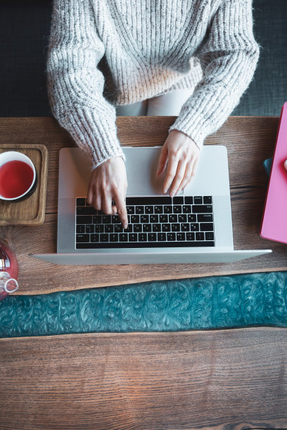 在咖啡馆里用笔记本电脑工作的女人喝着茶，俯视图。图片下载