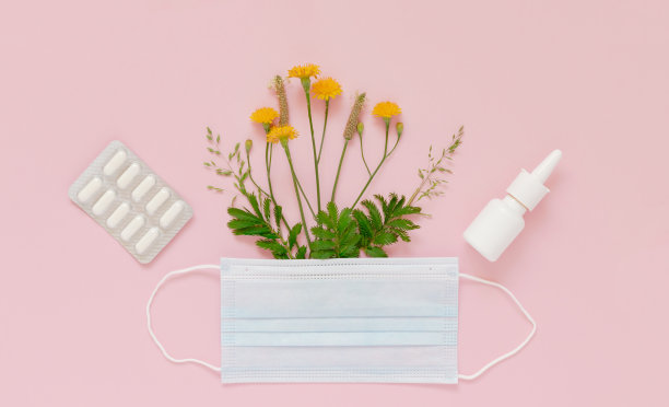 在一个保护面具下的野花和草本植物，一个鼻喷雾剂的模型和一个带有药片的水泡在浅粉色的背景上。季节性过敏的保护和治疗方法的概念。图片下载