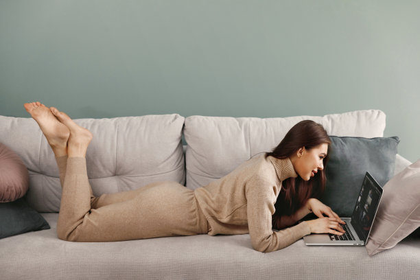 漂亮的年轻女人在沙发上用笔记本电脑工作。网上购物，支付，女商人使用笔记本电脑管理她的业务。图片下载