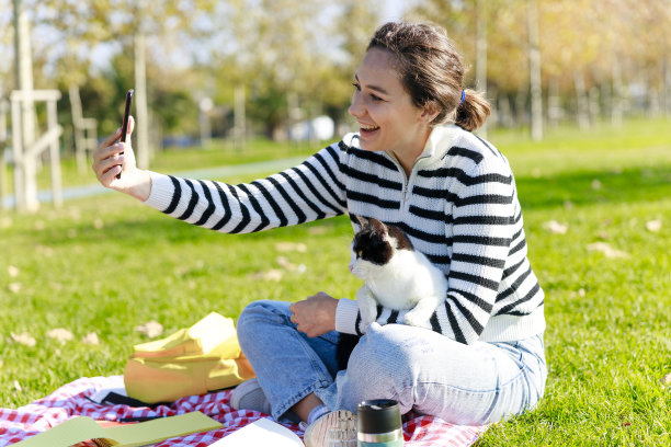 快乐的年轻女子和她的猫在户外的公园春天图片下载