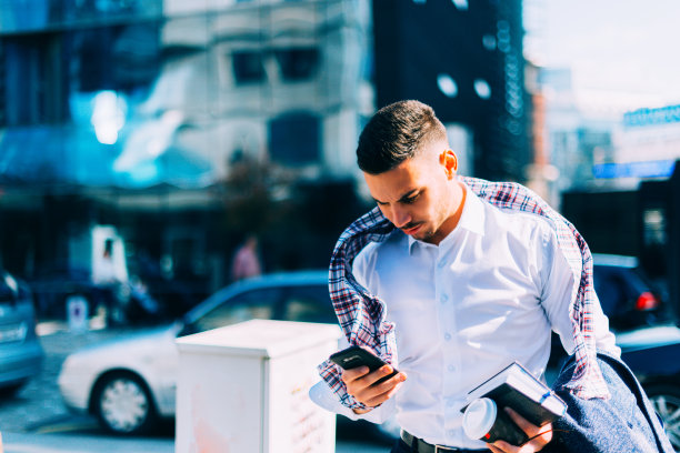 一个年轻的商人正走在市中心，手里拿着笔记本和咖啡，环顾四周图片下载