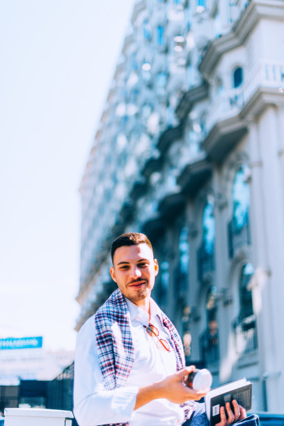 自信的商人走在城市的街道上，手里拿着咖啡和笔记本，享受着美好的天气。图片下载