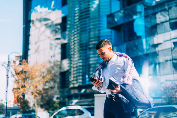 一个年轻的商人正走在市中心，手里拿着笔记本和咖啡，环顾四周图片下载